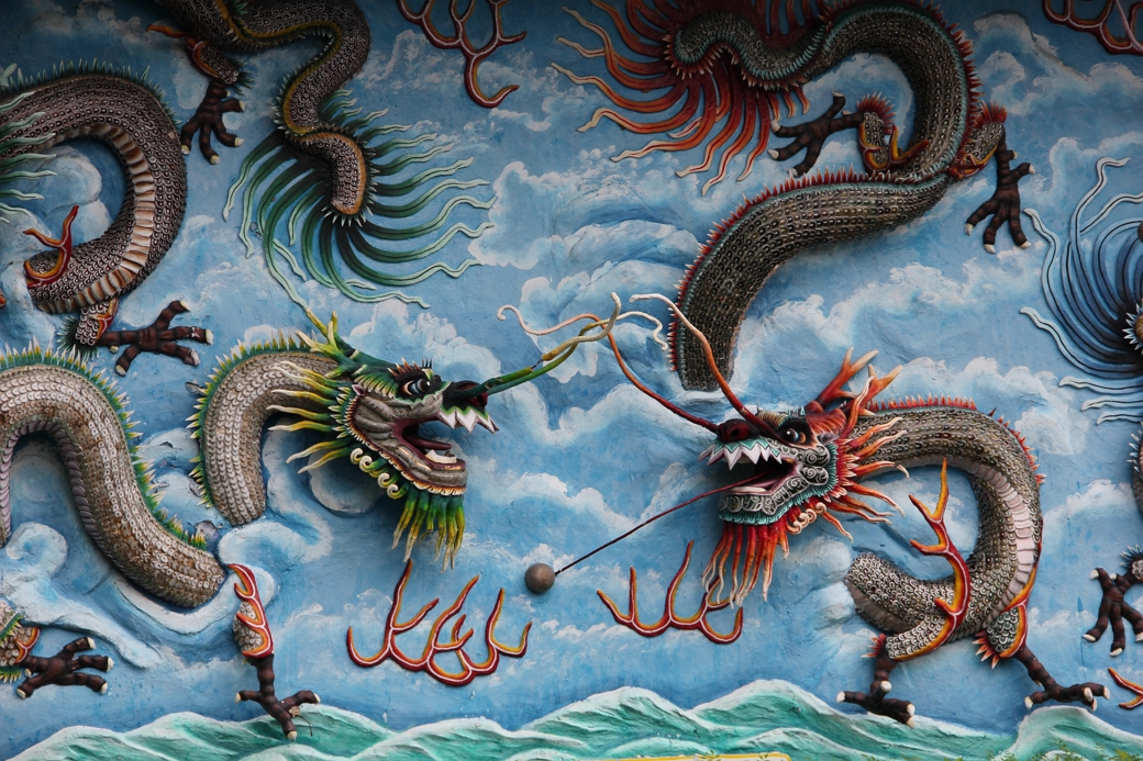 Reliƫf sculptuur van twee Chinese draken die uit de muur steken op een achtergrond van blauwe wolken en zee